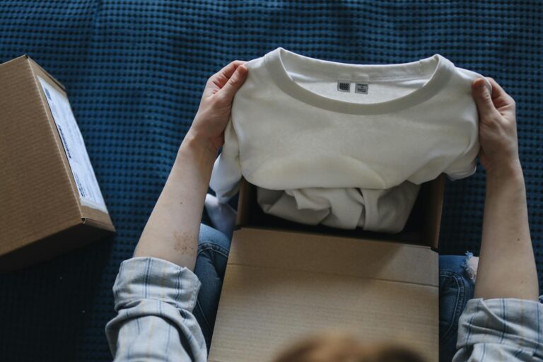 Close-up of hands opening a package containing a new white t-shirt indoors.