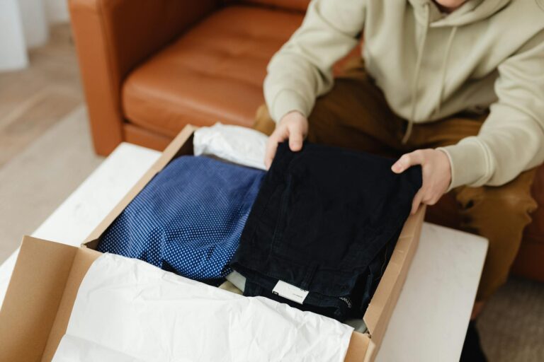 Man unboxing new clothes from a cardboard box on a table indoors.